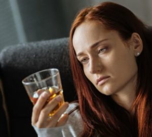 Smutna kobieta patrzy na szklankę alkoholu.