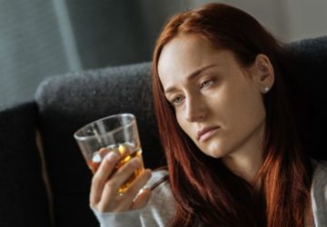 Smutna kobieta patrzy na szklankę alkoholu.