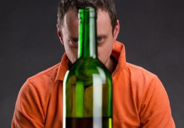 Alkoholik patrzący na butelkę z winem.