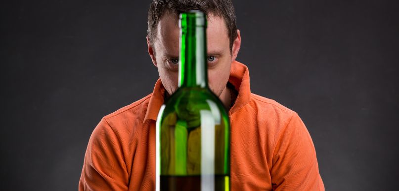 Alkoholik patrzący na butelkę z winem.
